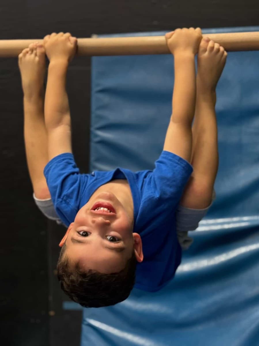 A boy hanging upside down from the bar, grinning